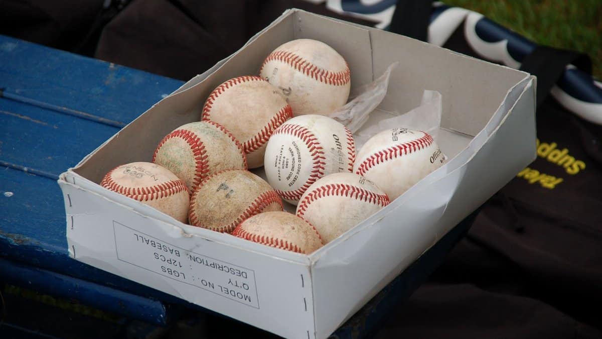 A box full of used baseballs sitting on a blue bench outdoors, perfect for sports enthusiasts.