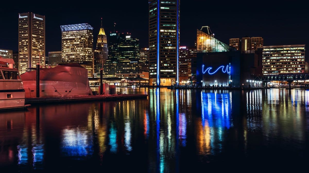 Vibrant Baltimore skyline at night with reflections on Inner Harbor water.