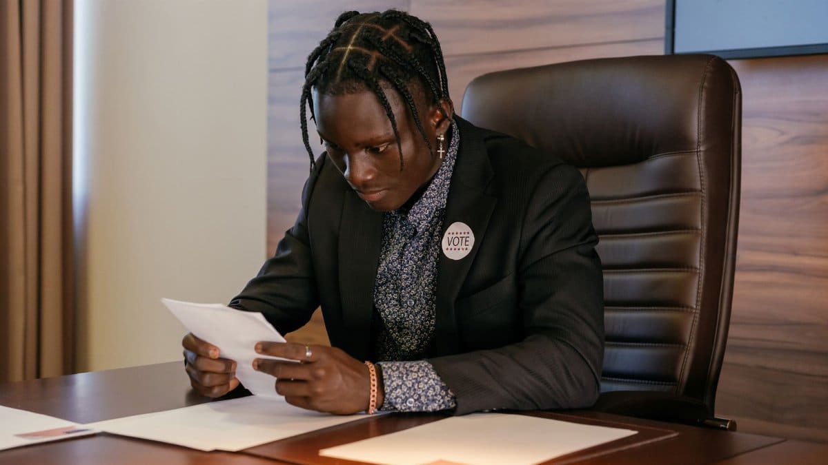Businessman in black suit reviewing papers at office desk, focused and engaged.