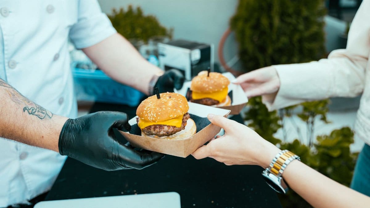 Chef hands over delicious cheeseburgers to a customer at an outdoor food stall.