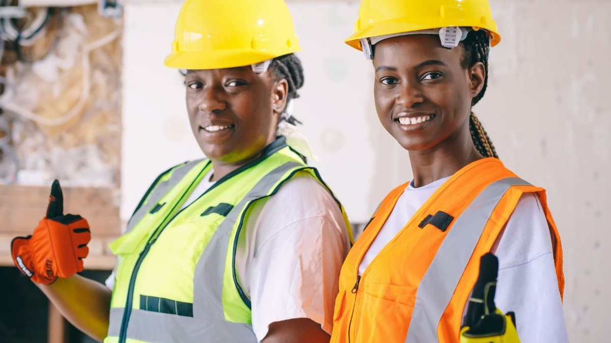 Two female construction workers wearing PPE, smiling and giving a thumbs up on site.