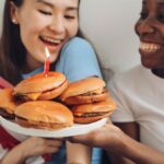 Two friends joyfully celebrating with burgers, laughter, and an American flag.