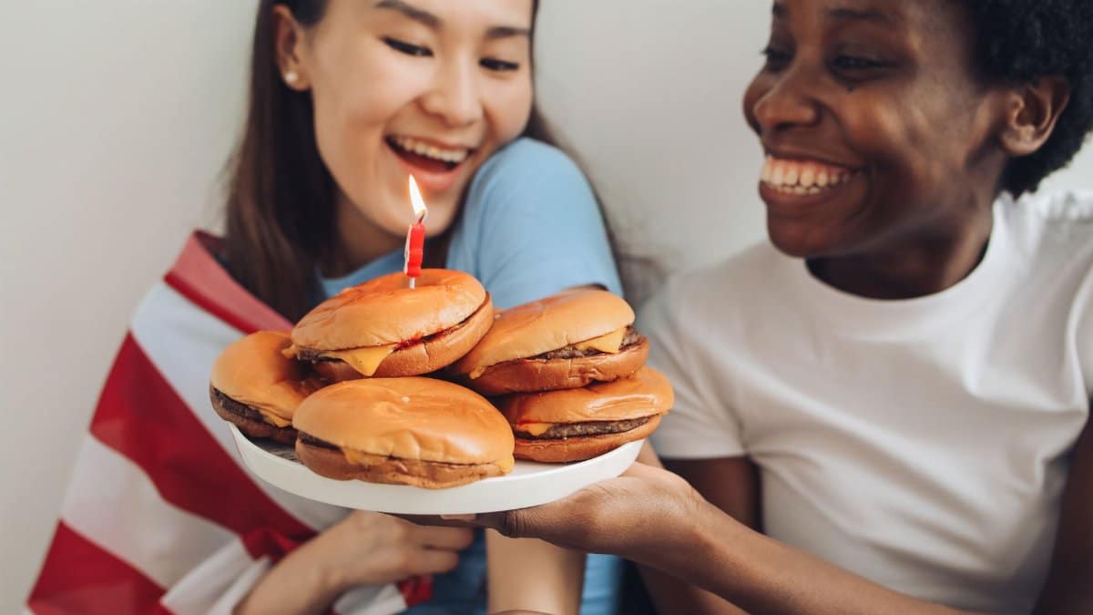 Two friends joyfully celebrating with burgers, laughter, and an American flag.