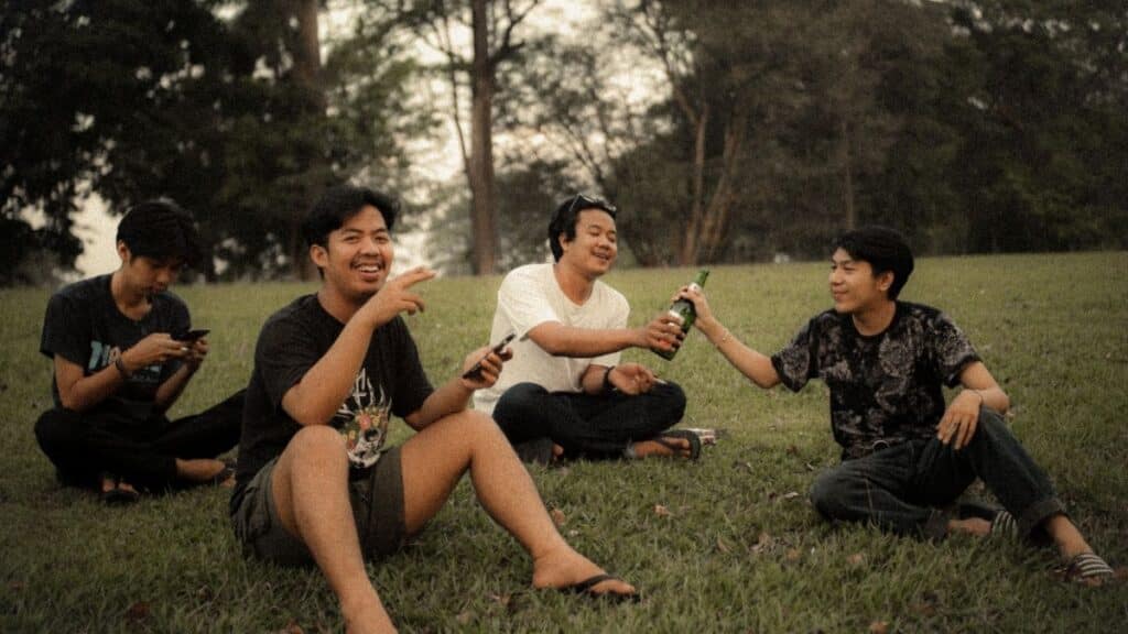 Group of friends enjoying drinks and laughter on a grassy field.