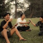 Group of friends enjoying drinks and laughter on a grassy field.