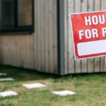 A modern wooden house with a prominent 'House for Rent' sign in the green yard.