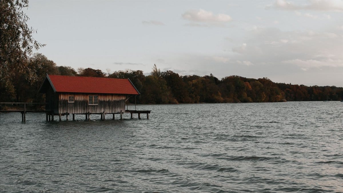Charming wooden boathouse on Ammersee Lake in Bavaria, framed by a serene autumn landscape.