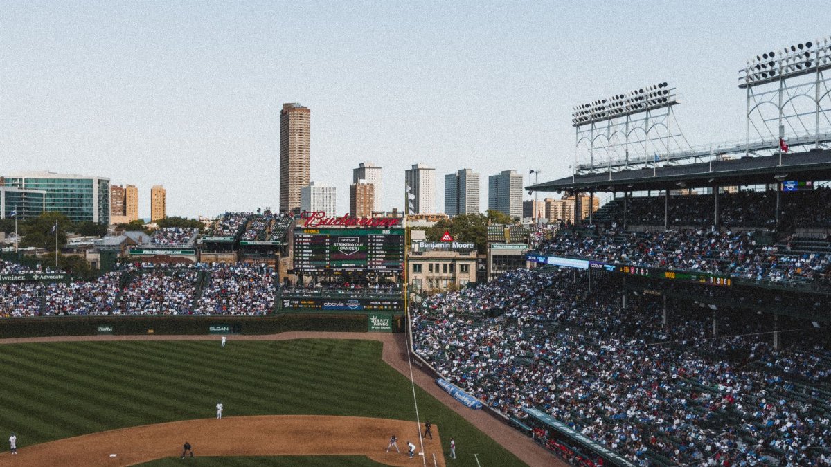 Crowded baseball stadium under a clear sky with cityscape background. Energetic game day atmosphere.
