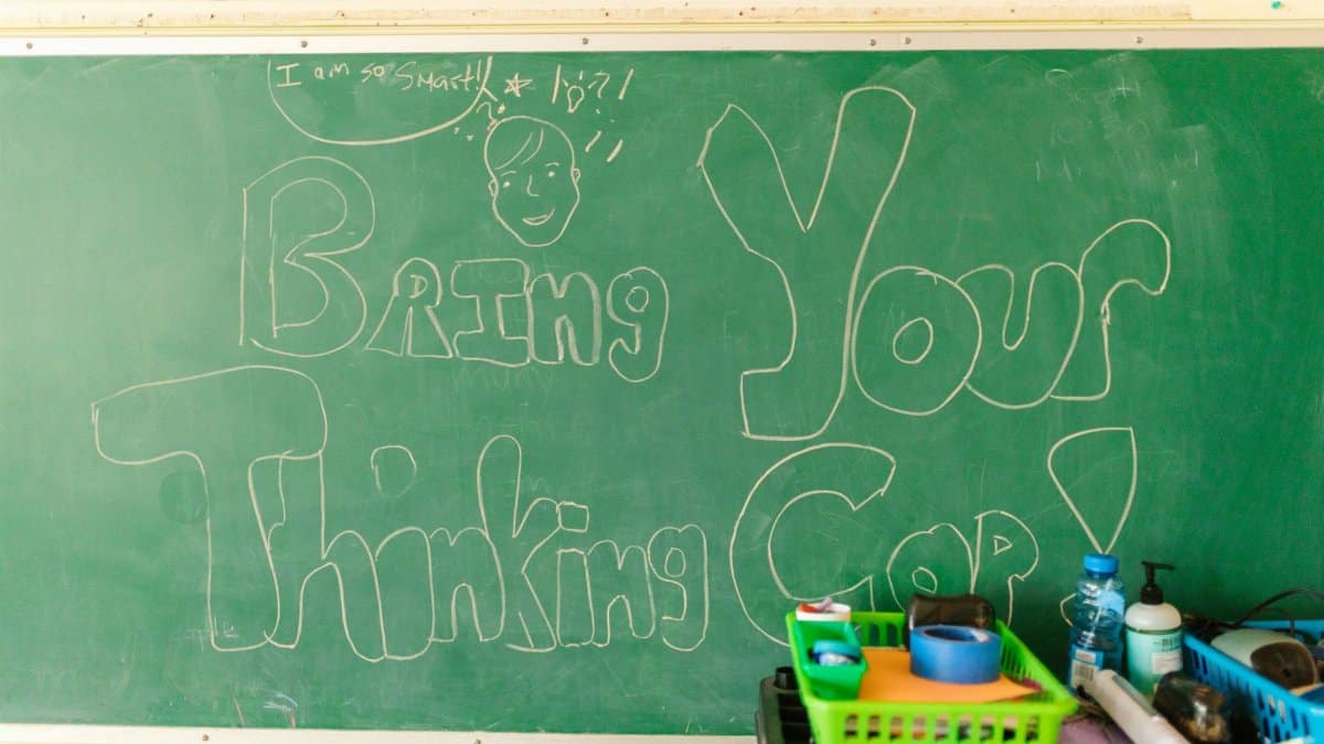 Classroom scene with chalkboard message "Bring Your Thinking Cap" and supplies.