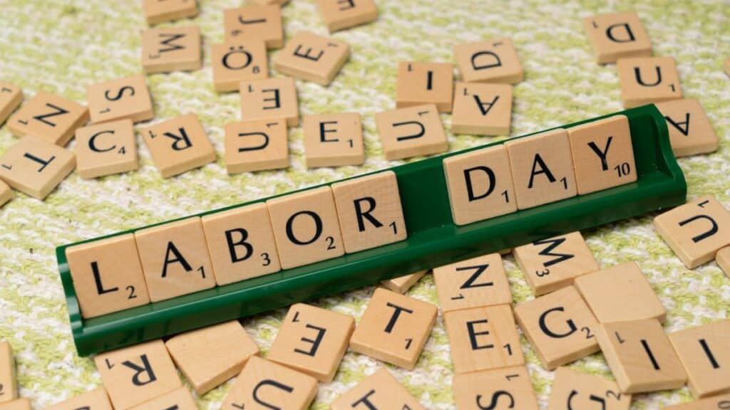 Scrabble tiles forming the phrase "Labor Day" on a green surface, symbolizing the holiday.