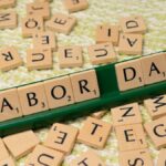 Scrabble tiles forming the phrase "Labor Day" on a green surface, symbolizing the holiday.