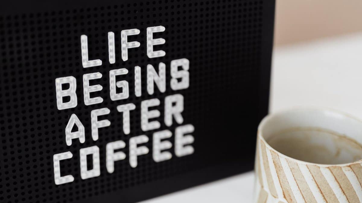 Peg message board with Life Begins After Coffee motto and empty ceramic cup of coffee with creative striped design on white table