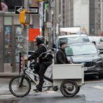Cyclist on delivery bike amidst busy New York City street with pedestrians and vehicles.