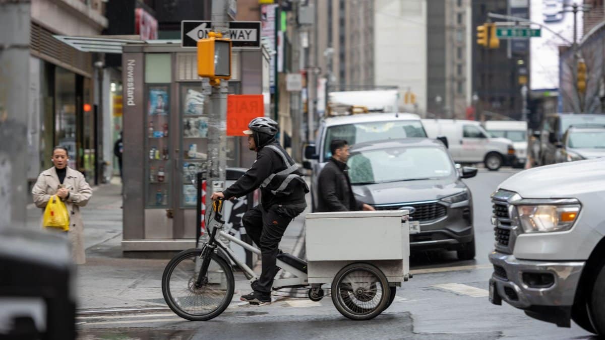 Cyclist on delivery bike amidst busy New York City street with pedestrians and vehicles.
