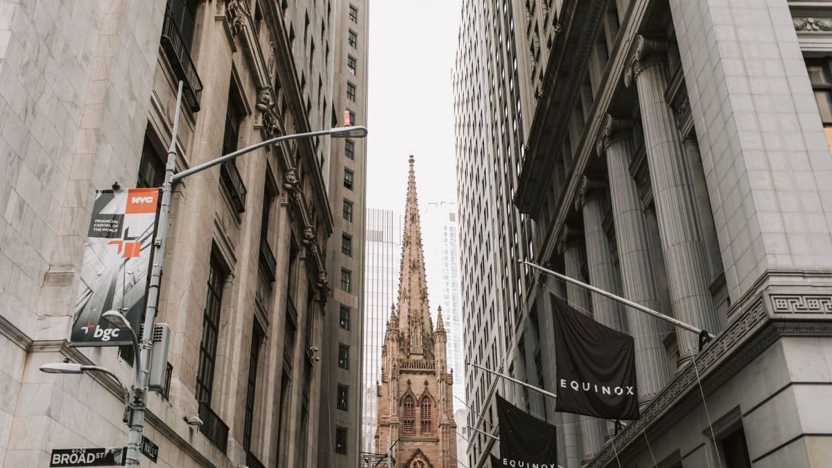 View of Trinity Church between skyscrapers on Broad Street, NYC, showcasing historic architecture.
