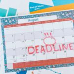 Vibrant August calendar on a desk with deadline marked in red, surrounded by graphs and charts.