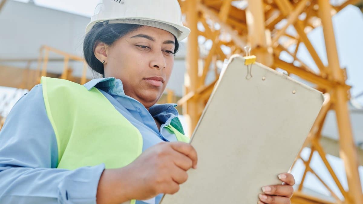 Confident female construction worker inspecting site with clipboard and helmet.