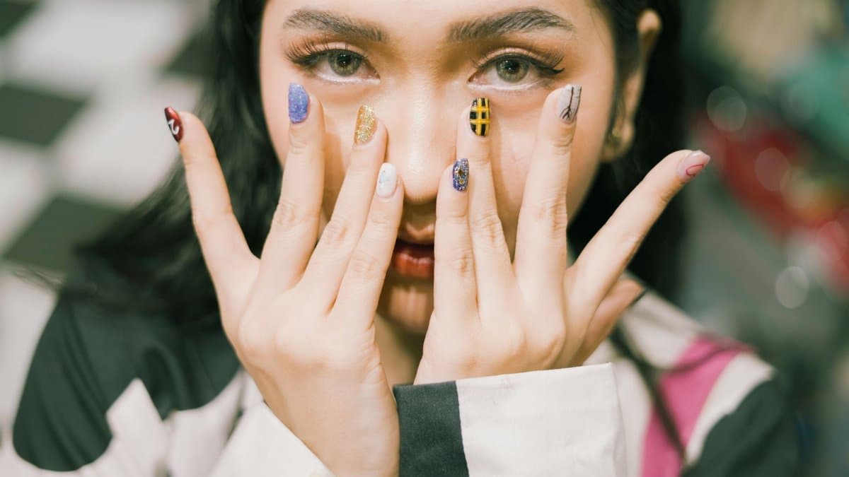 Close-up shot of a woman with colorful acrylic nails covering her face.