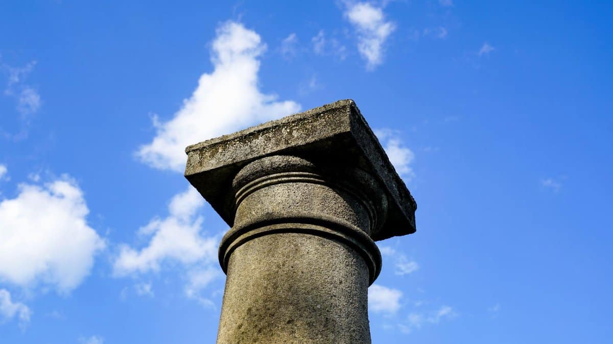 Low angle view of an ancient stone column with a clear blue sky and scattered clouds, evoking timeless architecture.