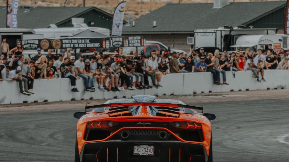 A stunning orange Lamborghini Aventador speeds at a race track with spectators in the background.