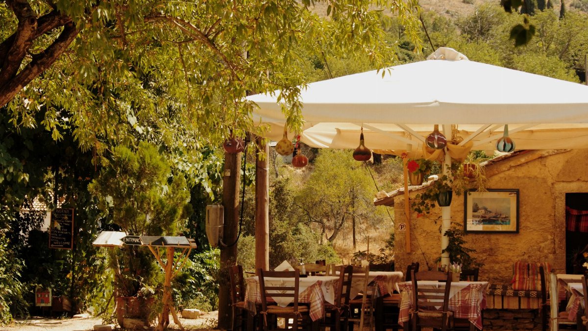 Charming outdoor seating at a Grecian tavern in Perithia, Greece, surrounded by lush greenery.