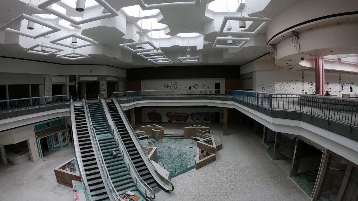 Desolate interior of an abandoned shopping mall with broken escalators and graffiti-covered walls.