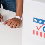 A person casting a vote with a ballot near a marked voting box, emphasizing civic participation.