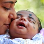 Heartwarming portrait of a mother kissing her smiling baby outdoors.
