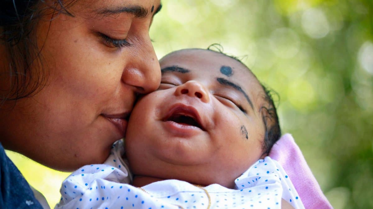 Heartwarming portrait of a mother kissing her smiling baby outdoors.
