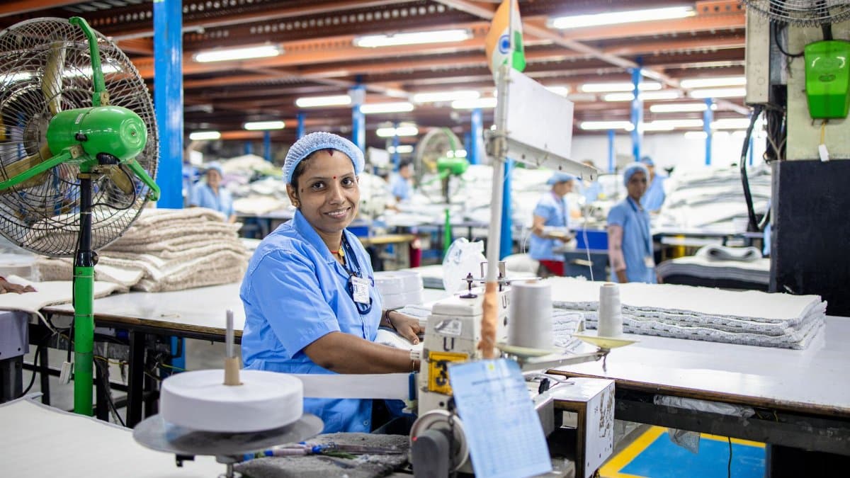 A female factory worker in India manages a sewing machine in a bustling textile factory.
