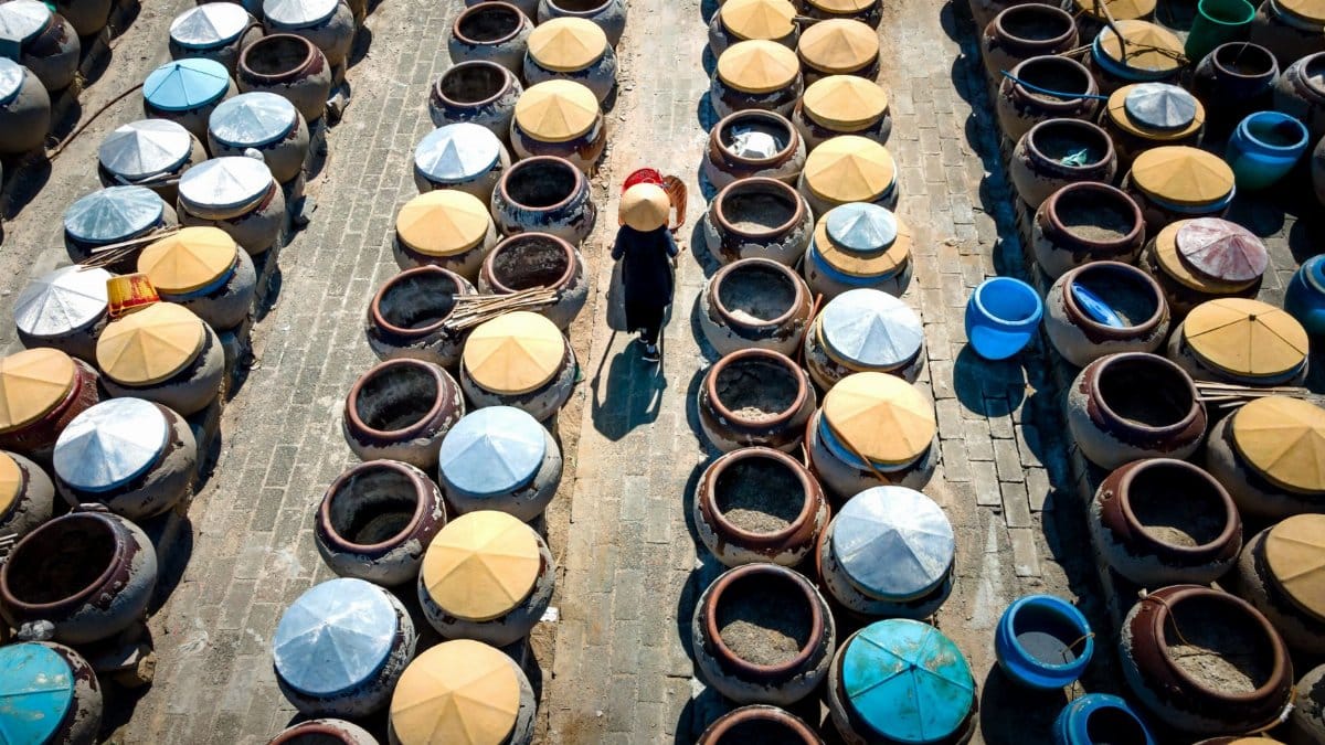 Aerial shot of a worker walking through rows of colorful clay pots in bright sunlight.