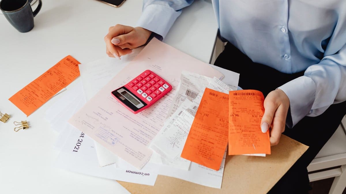 A woman reviews receipts and calculates expenses at a desk with a pink calculator.