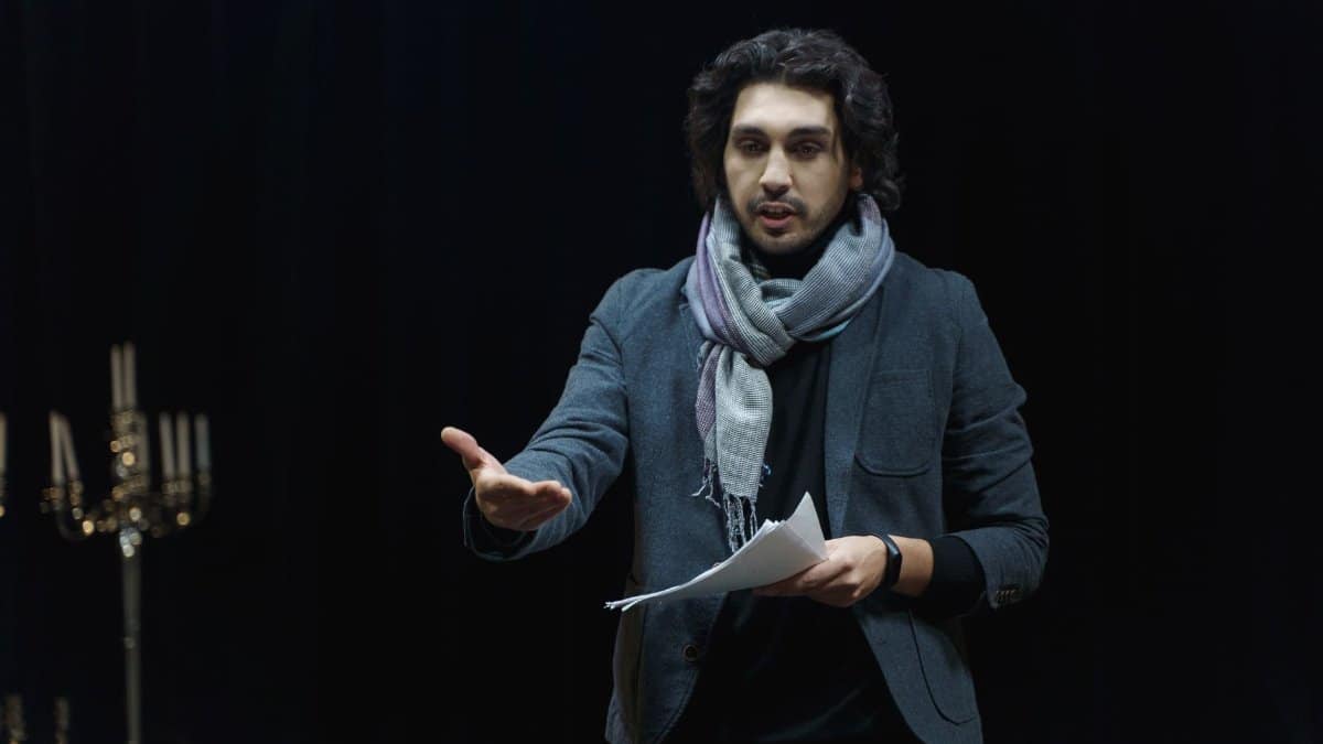 Actor rehearsing on a dark theater stage, holding a script and gesturing dynamically.
