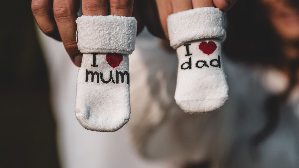 Close-up of parents holding baby socks indicating pregnancy announcement, tagged with 'I love mum' and 'I love dad'.