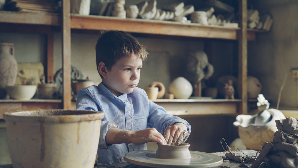 A young boy focused on molding clay on a potter's wheel in a pottery workshop.