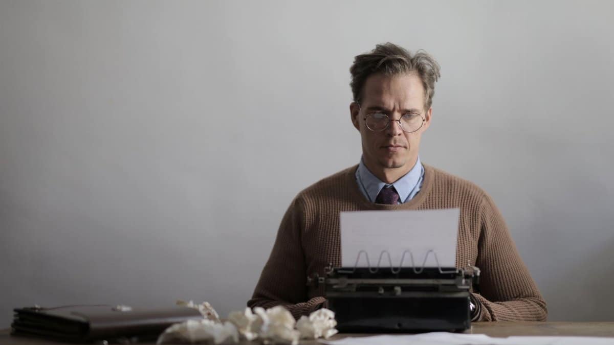 A thoughtful male writer typing on a vintage typewriter, surrounded by crumpled papers.