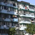 Exterior view of urban apartments with laundry hanging outside on balconies under a clear sky.