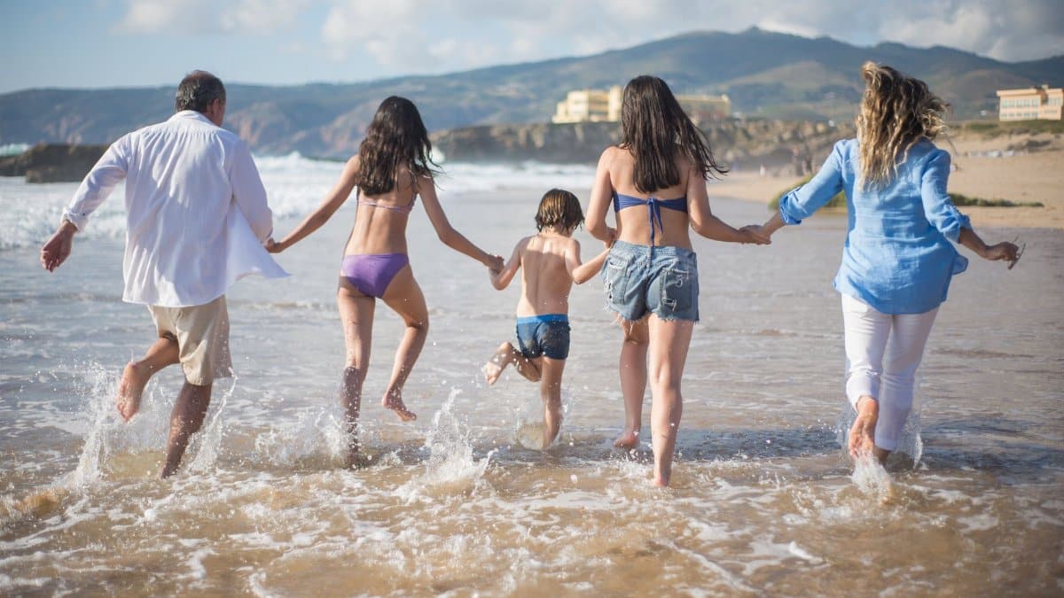 A family having fun running into the ocean on a sunny beach day in Portugal. Joyful and carefree moments.