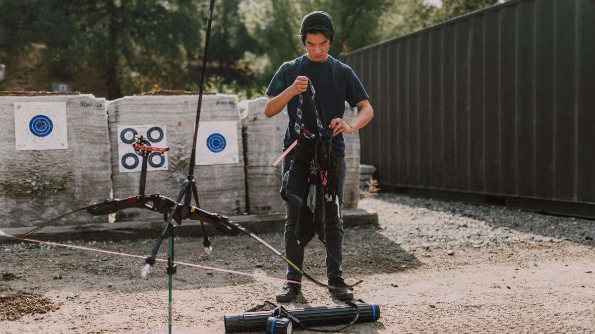 Teen adjusting equipment at an outdoor archery range, a focus on youth archery practice.