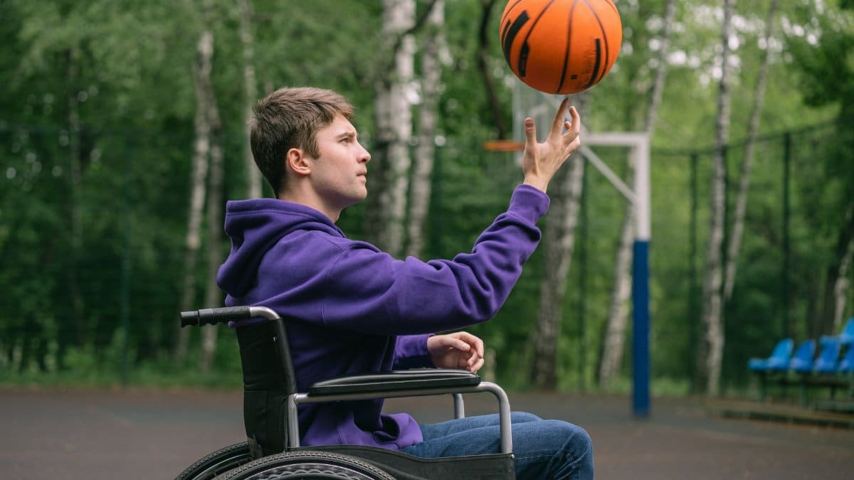 A man in a wheelchair skillfully spinning a basketball on his finger outdoors.