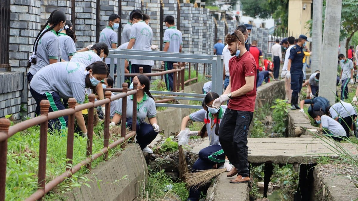 Group of volunteers in masks participating in outdoor canal cleanup effort.