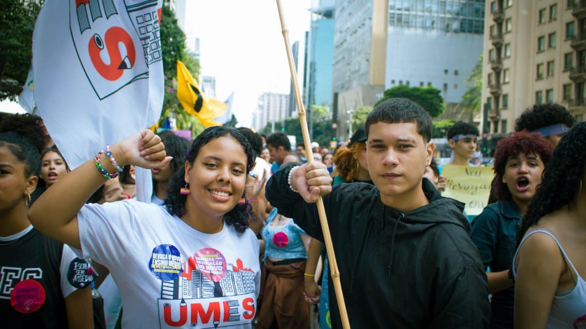 Energetic youth protestors holding flags and signs during a daytime urban demonstration.