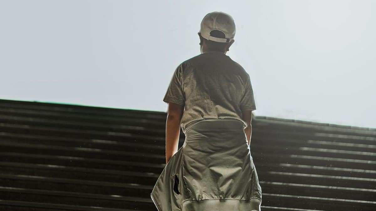 A youth wearing casual attire stands on outdoor stairs under daylight, evoking a sense of contemplation.