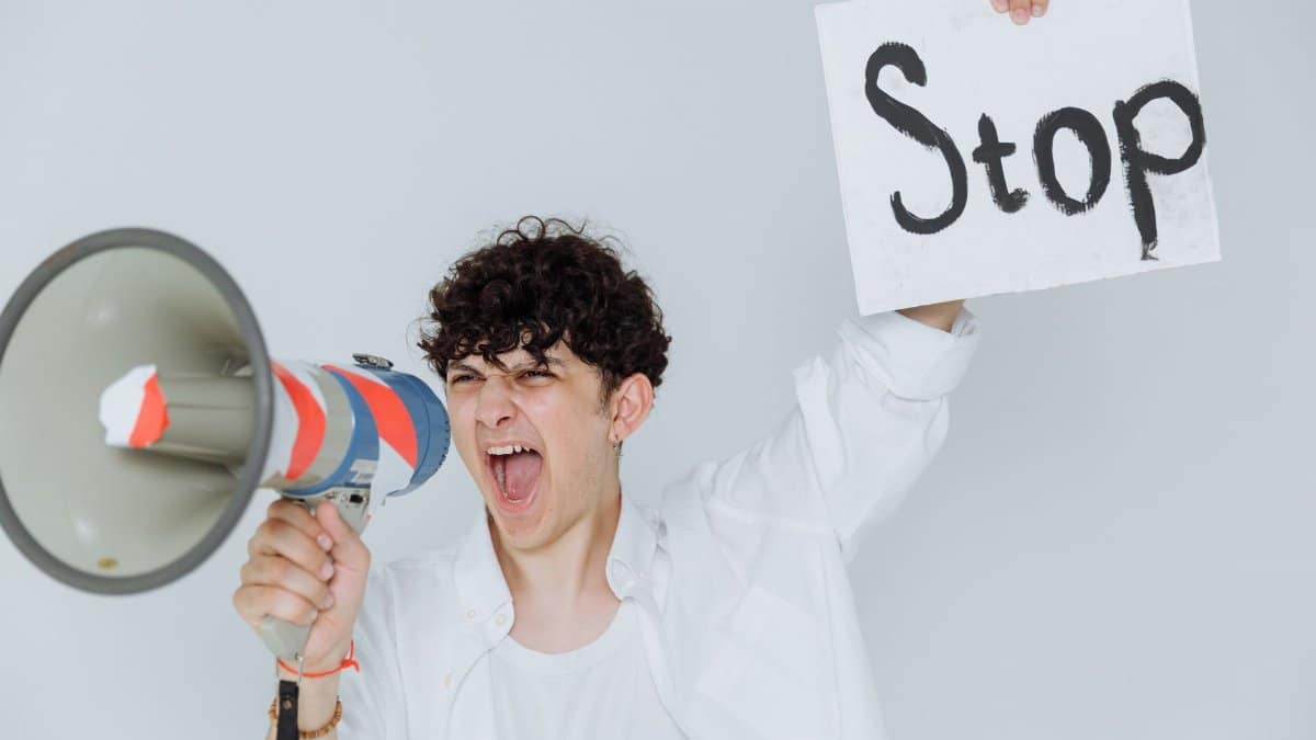 Person passionately expressing a protest message using a megaphone and a 'Stop' sign.