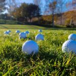 Golf balls scattered on a lush green course under a clear blue sky.