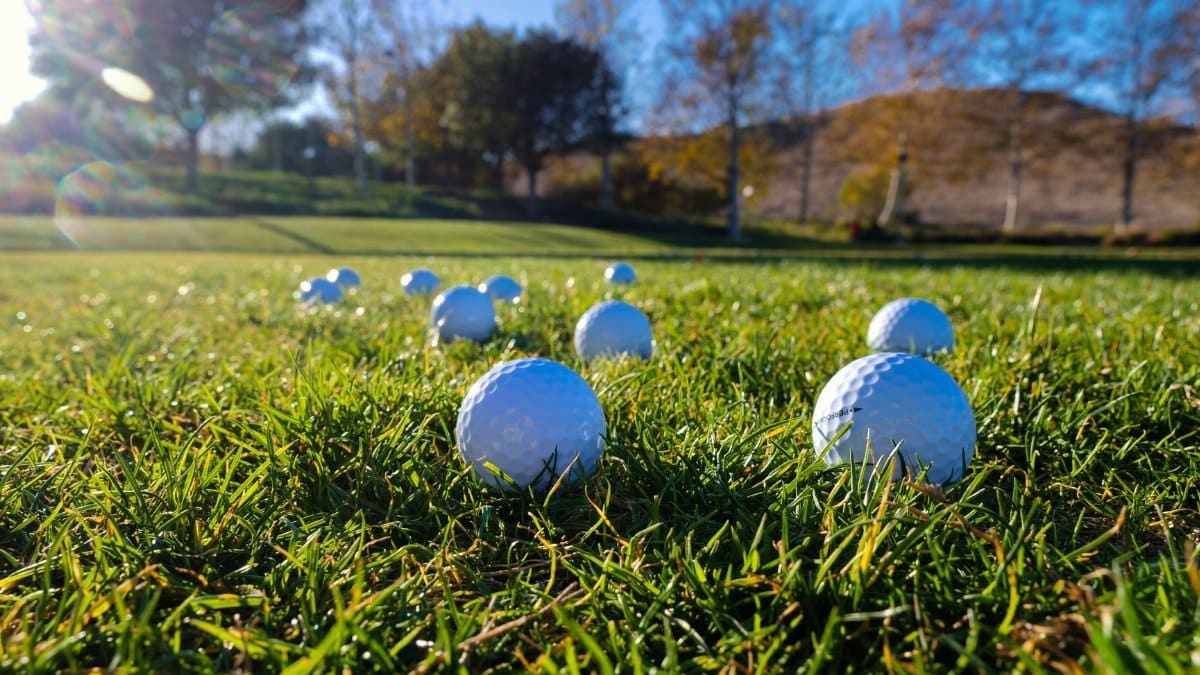 Golf balls scattered on a lush green course under a clear blue sky.