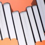 Stack of black hardcover books aligned against a vibrant orange backdrop, viewed from above.
