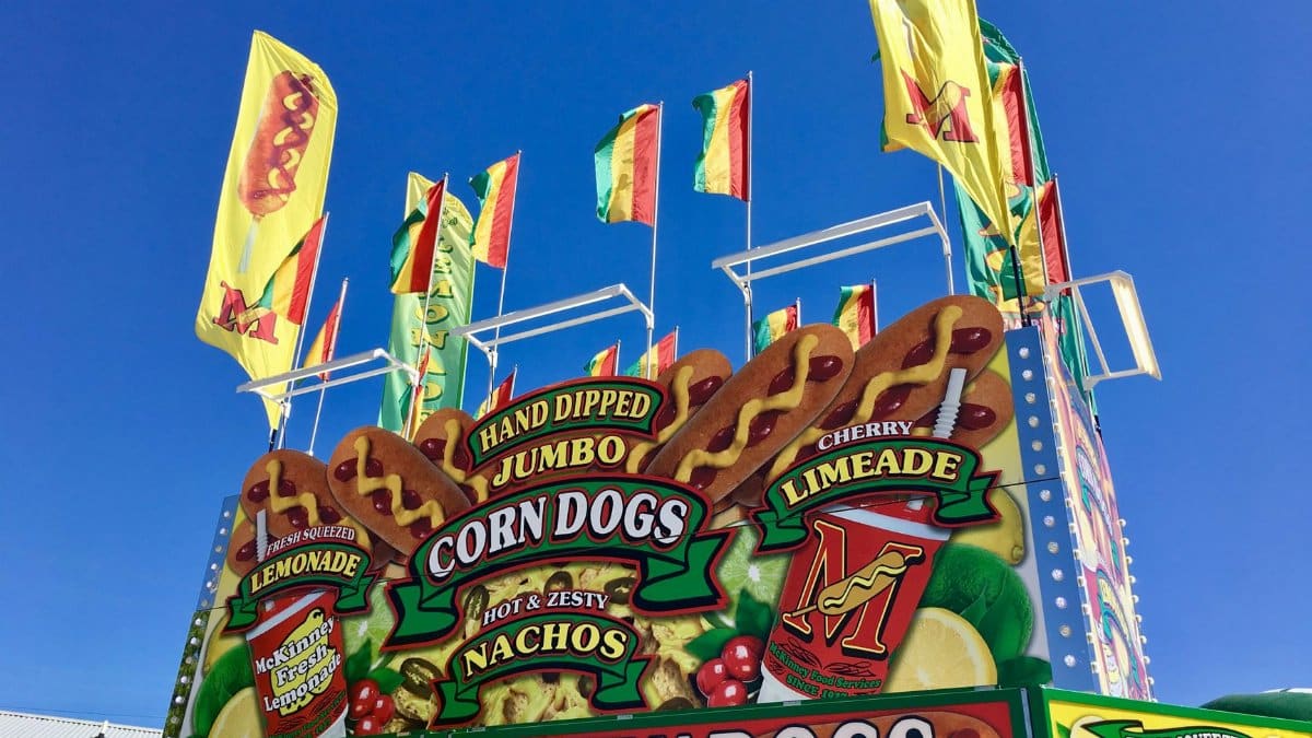 Vibrant fair stand in Grapevine, TX with corn dogs, lemonade, and flags under clear skies.