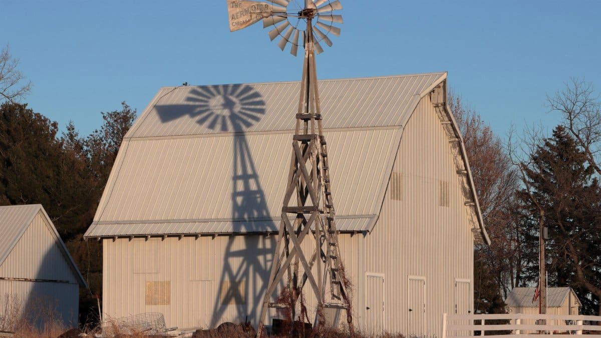 A classic rural scene featuring a barn and a traditional windmill under a blue sky.