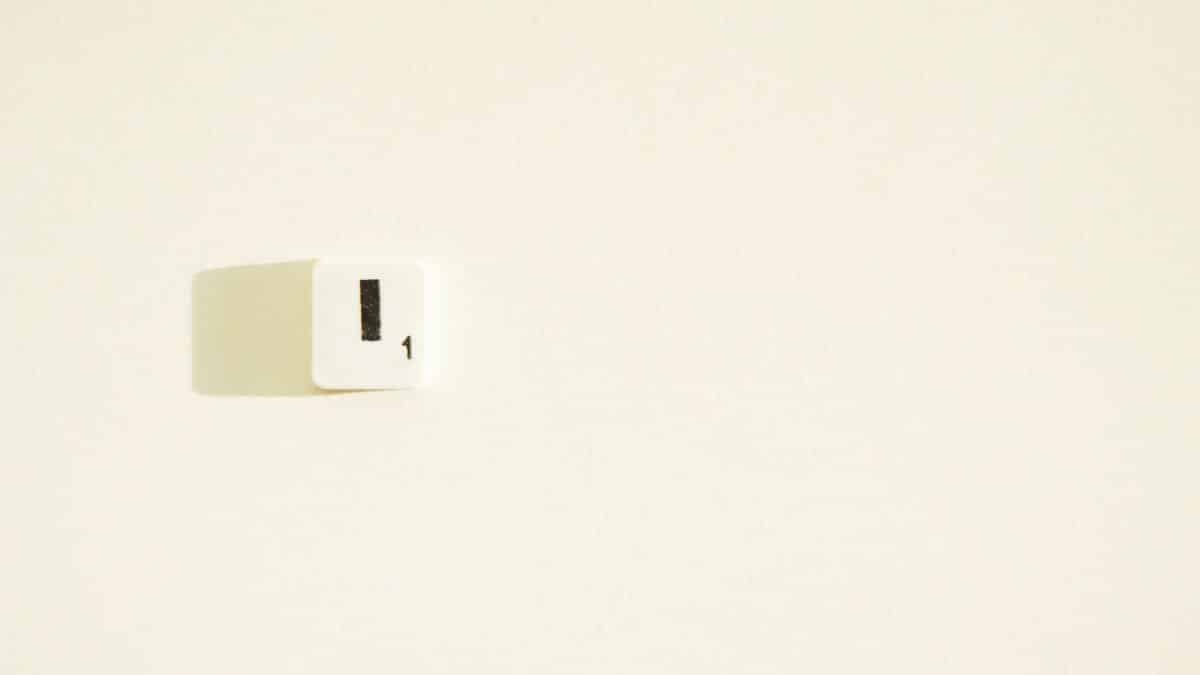A white Scrabble tile with the letter 'I' and number '1' with a shadow on a light wall.